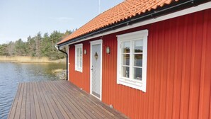 Punainen puinen rakennus, jossa on tiilikatto, puinen terassi ja taustalla näkyy vesistö.