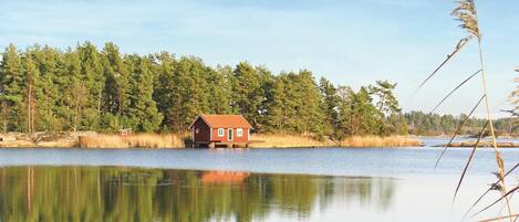 A cabin by a calm lake surrounded by dense forest.