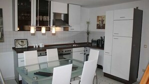 Une cuisine moderne avec des meubles blancs, une table à manger en verre et des luminaires suspendus.