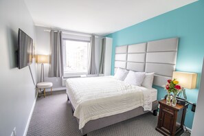 Een hotelkamer met een groot bed, een nachtkastje met een lamp, een aan de muur bevestigde televisie en een raam met gordijnen.