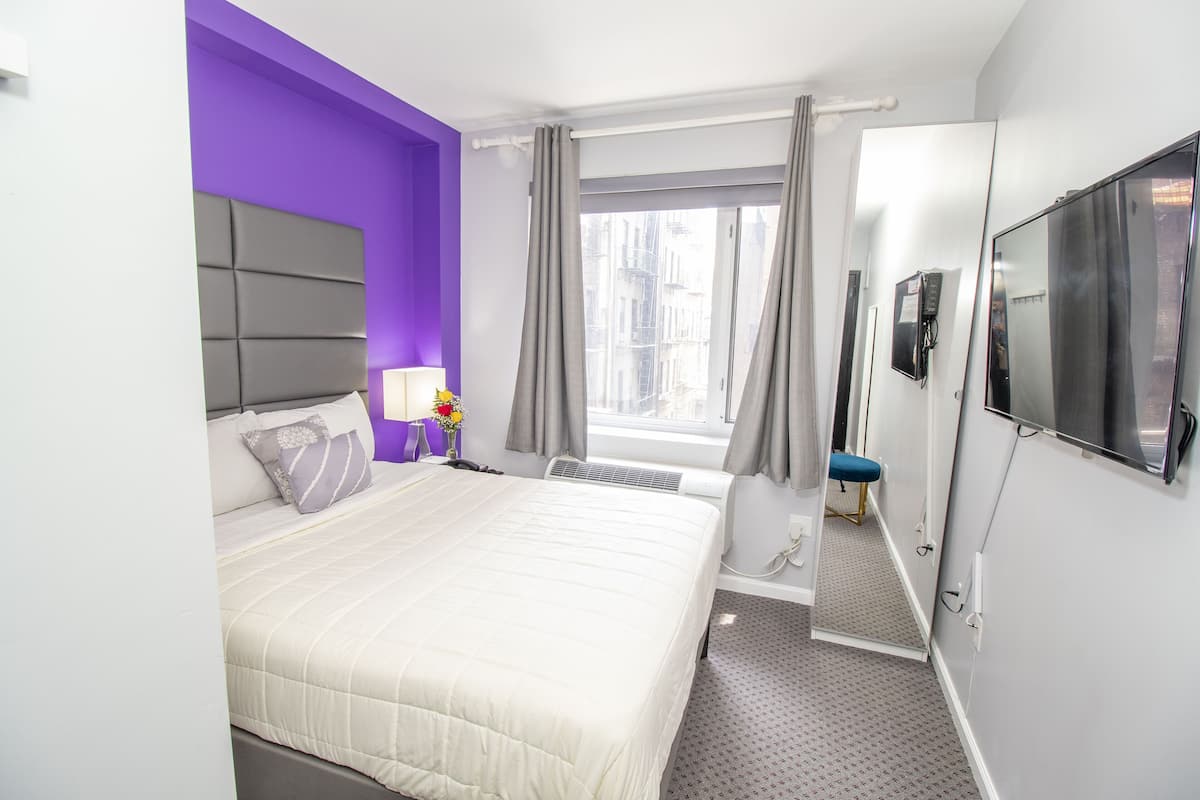 A hotel room with a bed, a TV, a window with curtains, and a bathroom visible through the door.