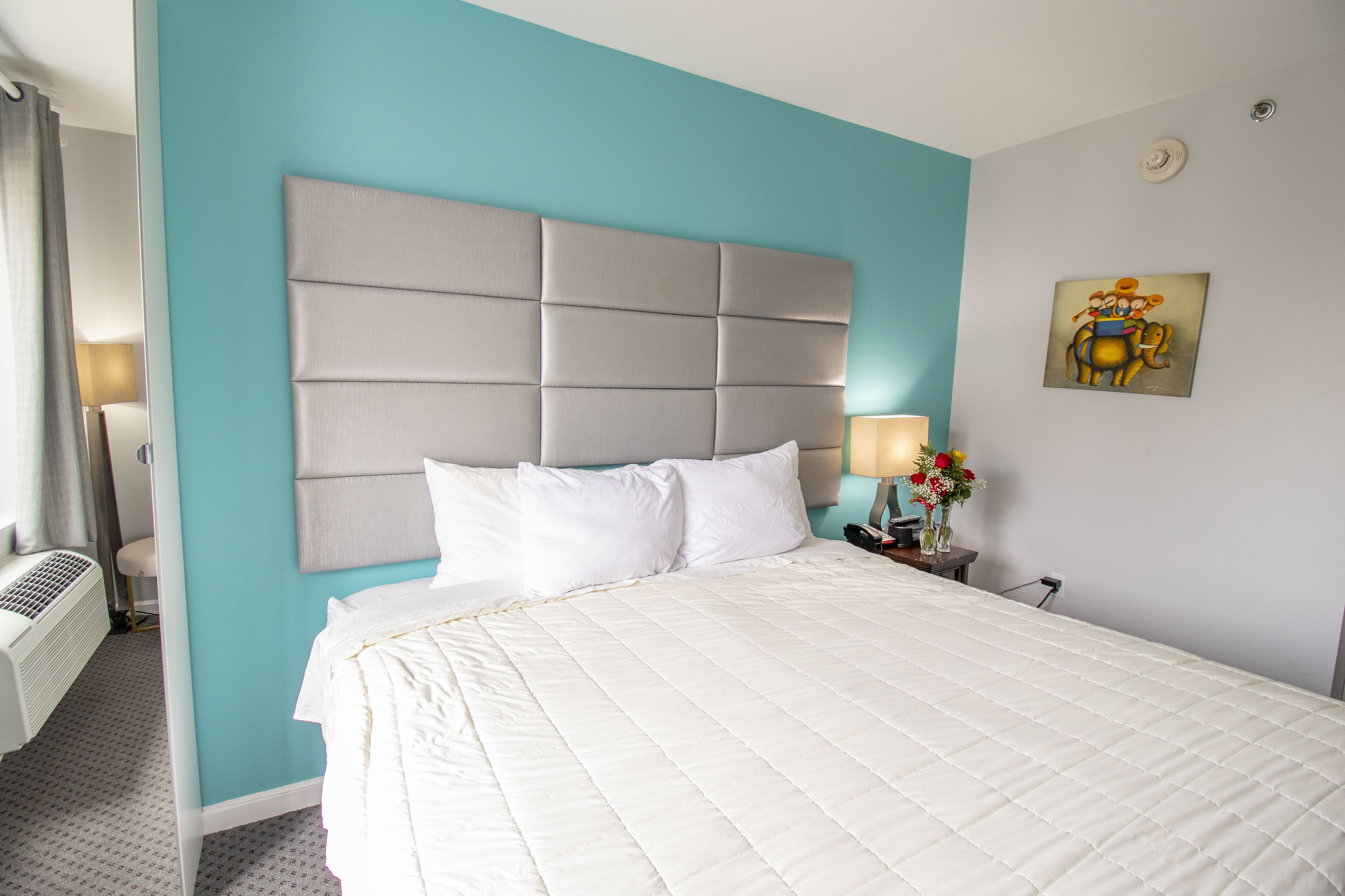 Een hotelkamer met een groot bed, een hoofdbord, een nachtkastje met een lamp en een schilderij aan de muur.
