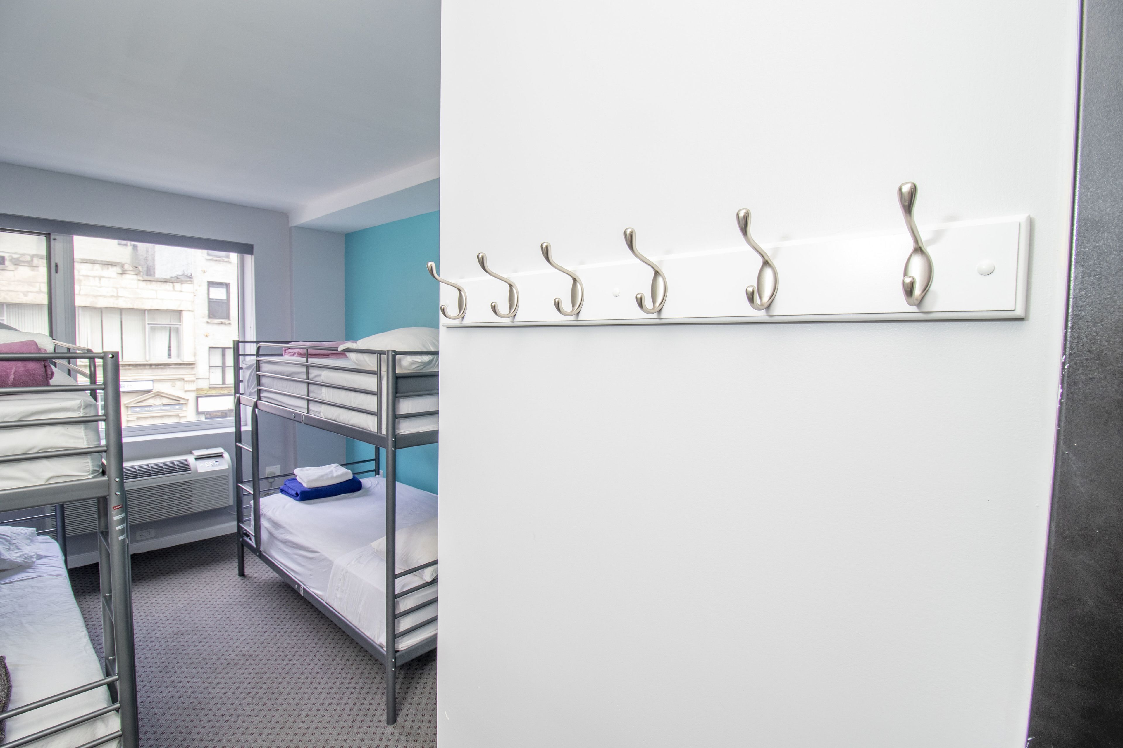 A dormitory room with bunk beds, a window, and a wall-mounted coat rack.