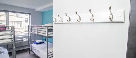 A dormitory room with bunk beds, a window, and a wall-mounted coat rack.