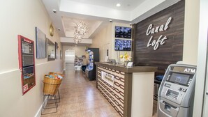 A reception area with a reception desk, an ATM, and a wall-mounted TV displaying multiple screens. - Canal Loft Hotel (New York)