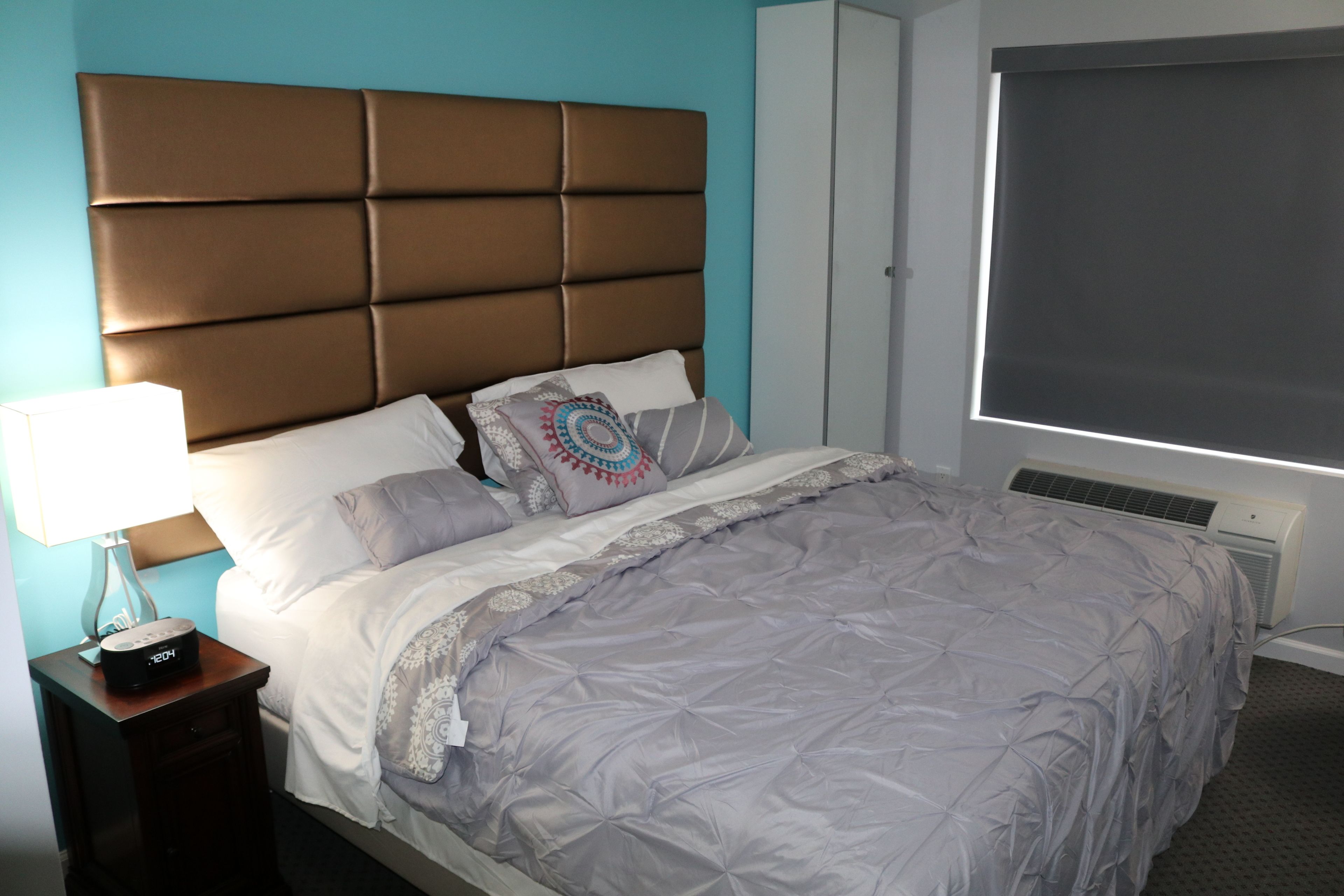 Un dormitorio con una cama grande, una mesita de noche con lámpara y una ventana con persianas.