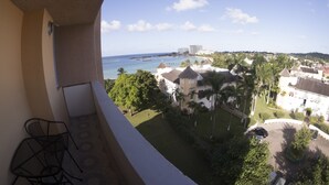 A balcony with a view of a beach, palm trees, and buildings. - Beach Condo at Turtle Towers (Ocho Rios)