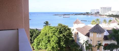 A coastal hotel with a view of the sea, palm trees, and a building with a tower.