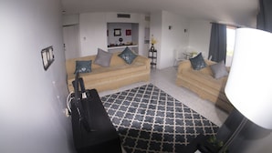 A living room with two sofas, a coffee table, and a TV. There is a patterned rug on the floor and a plant on a side table. - Beach Condo at Turtle Towers (Ocho Rios)