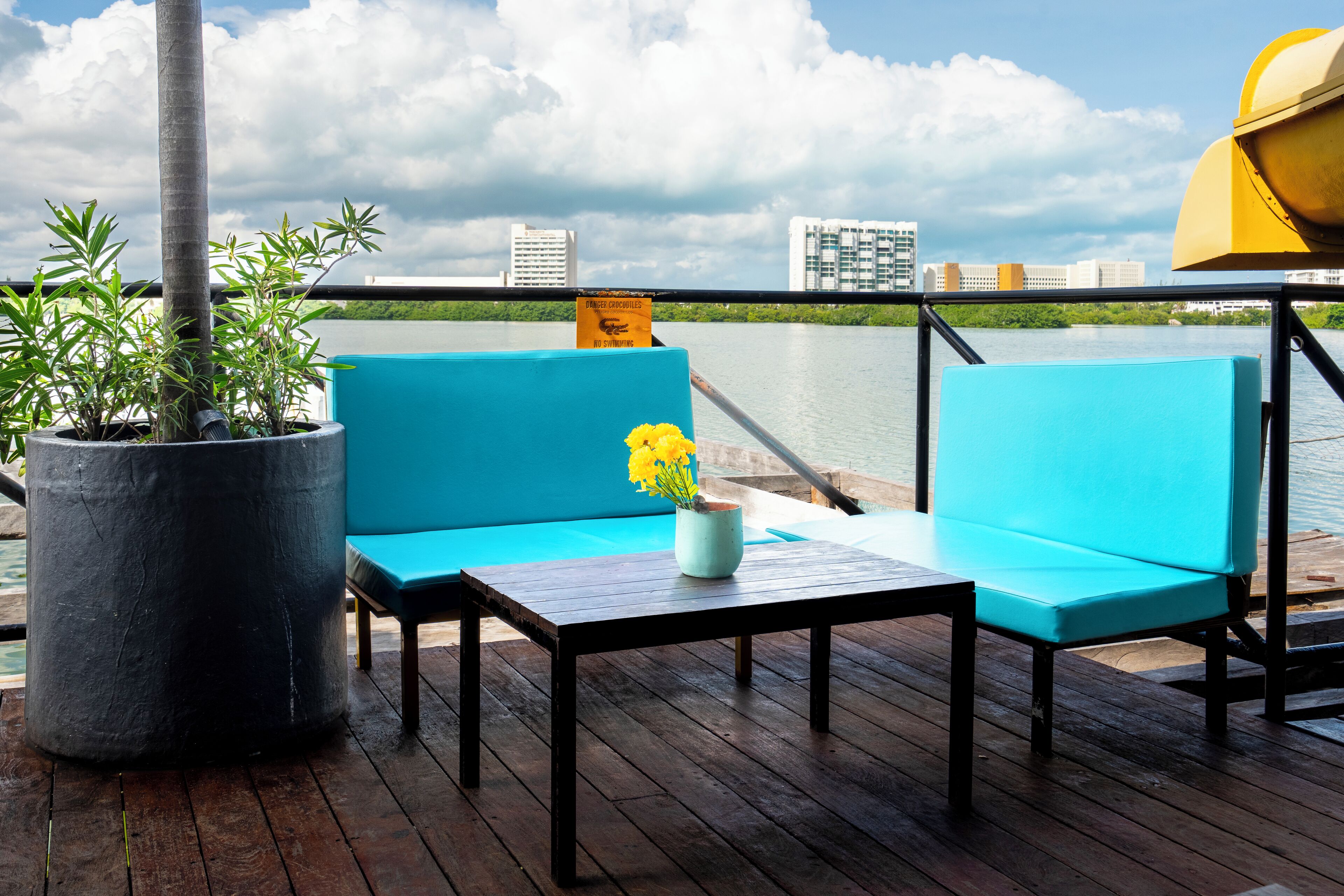 A deck with a blue sofa and a table, a potted plant, and a yellow sign.
