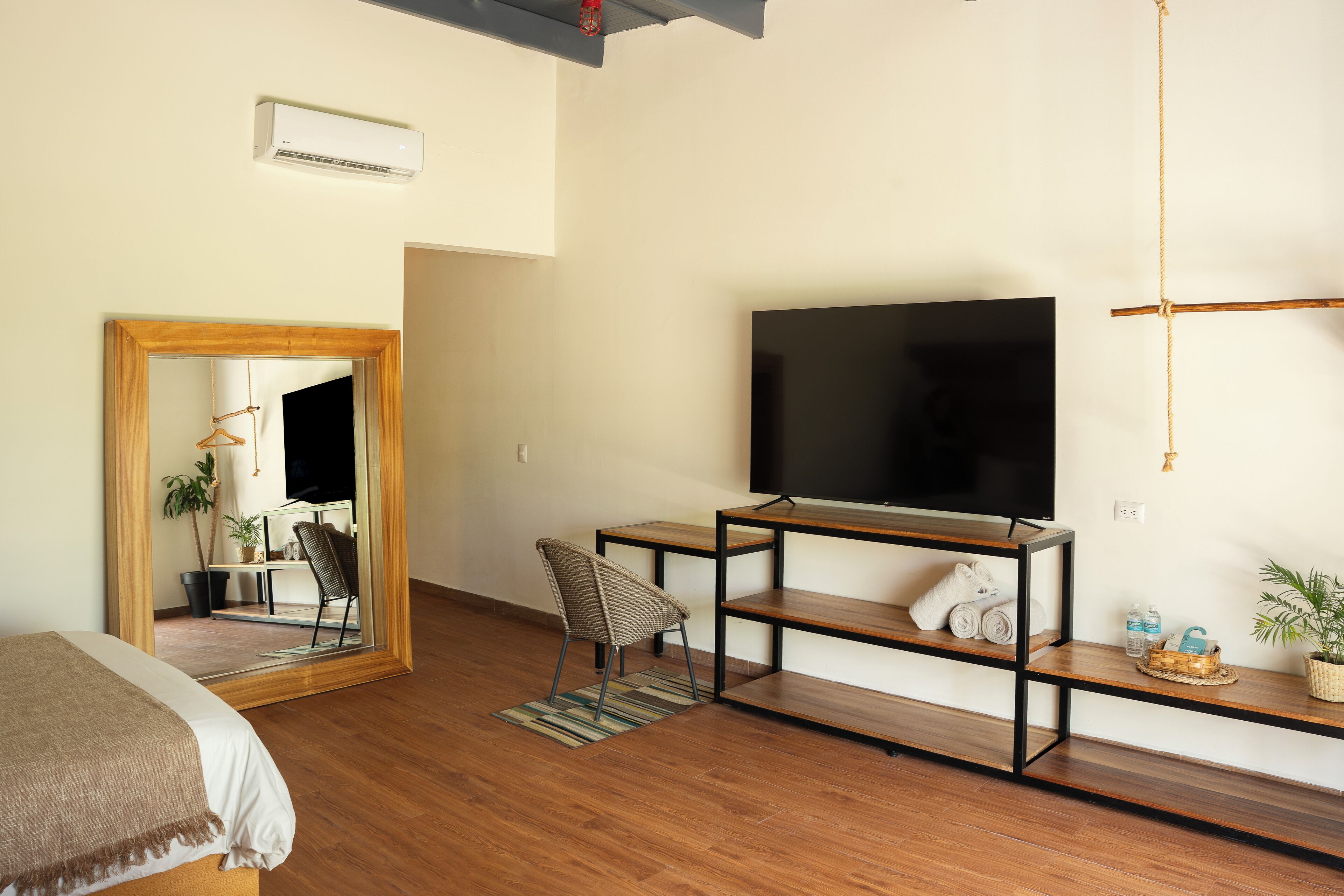 A modern living room with a large mirror, a flat-screen TV, a wooden floor, and a small seating area.