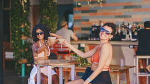 Dos personas sentadas en una mesa de madera al aire libre, sosteniendo bebidas.