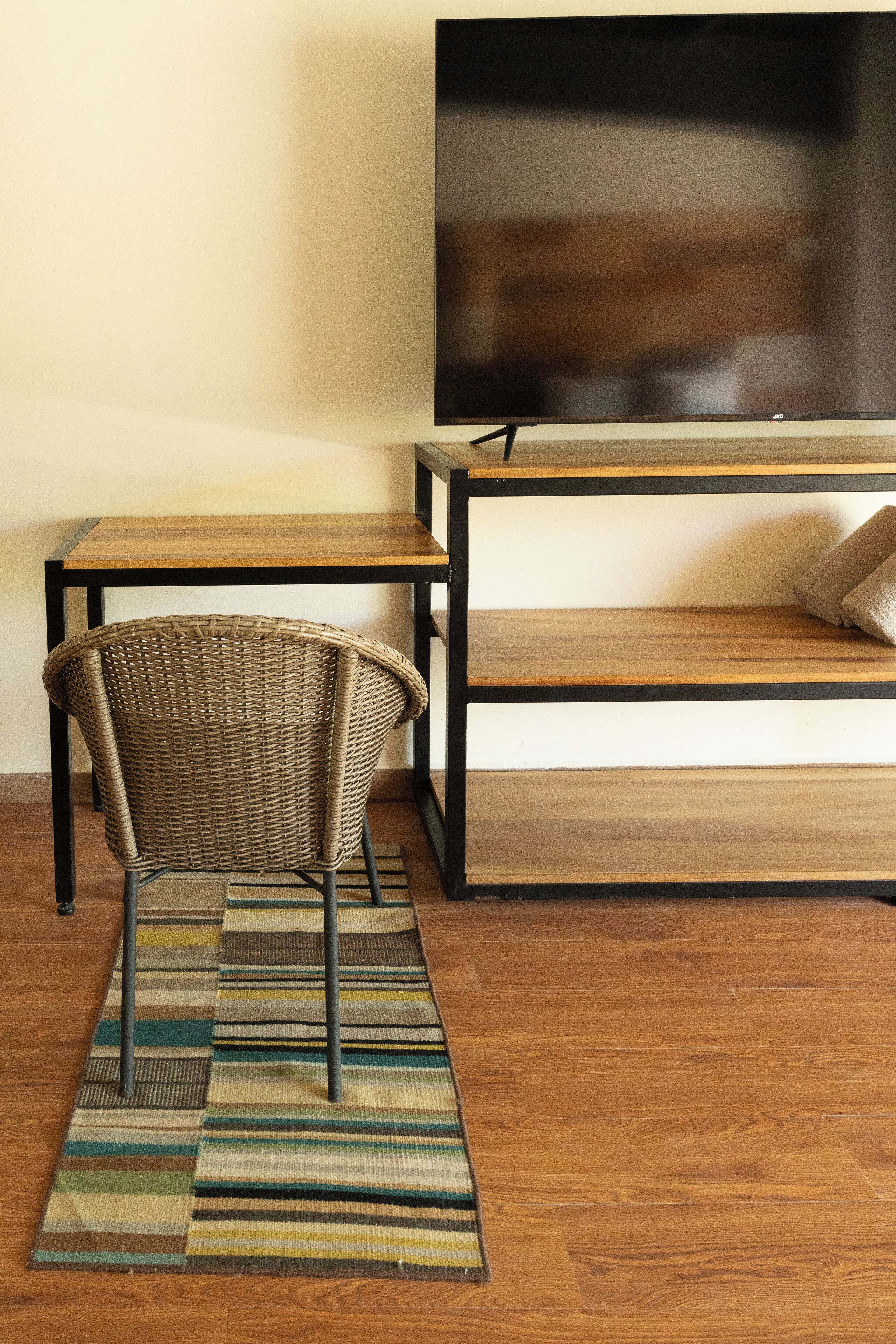 A room with a wicker chair, a wooden table, a TV on a stand, and a striped rug.