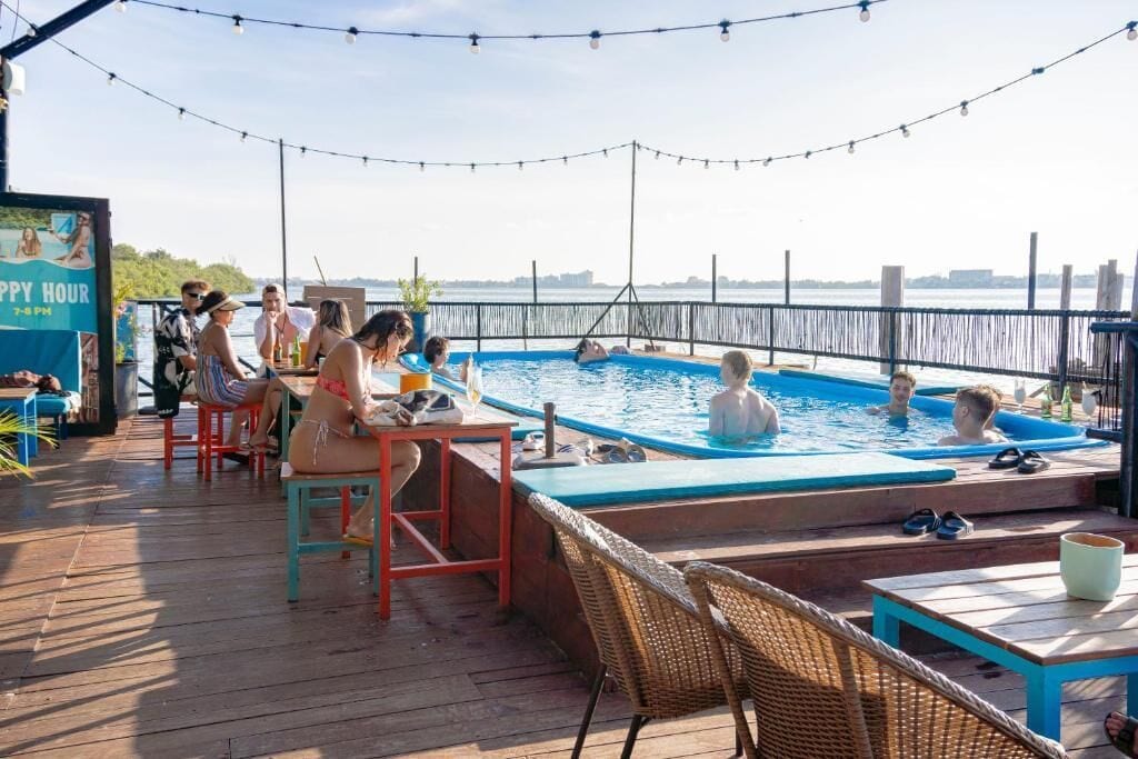 A poolside area with a wooden deck, seating, and a sign that reads "Happy Hour 7-9 PM".