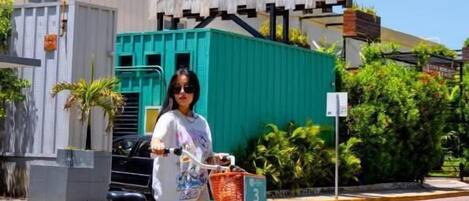 Una persona de pie junto a una bicicleta turquesa con una canasta, frente a un edificio con un letrero que dice "MAYAN MONKEY".
