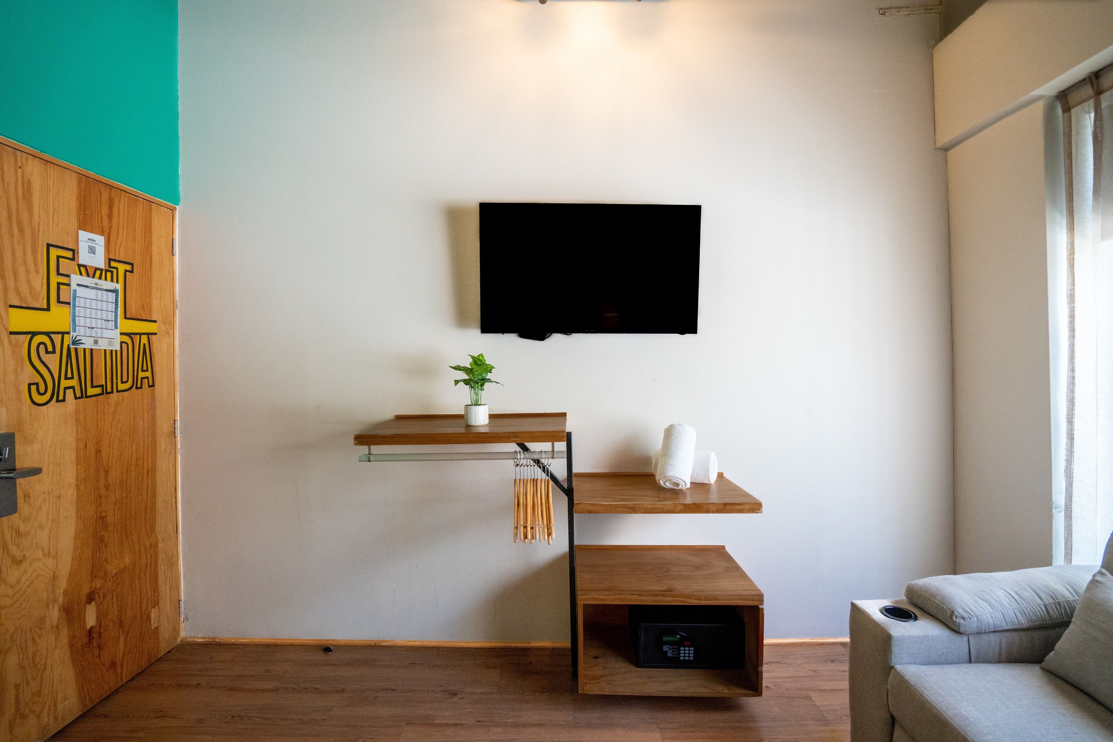 Una sala de estar moderna con un televisor montado, estanterías de madera, una planta pequeña y un sofá gris.