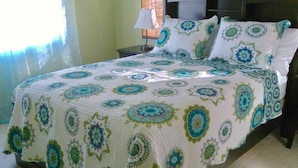 Een bed met een bedspread met patroon, een nachtkastje met een lamp en een raam met gordijnen.