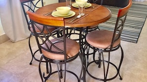 Een eetgedeelte met een ronde houten tafel, vier stoelen en een bankstel op de achtergrond.