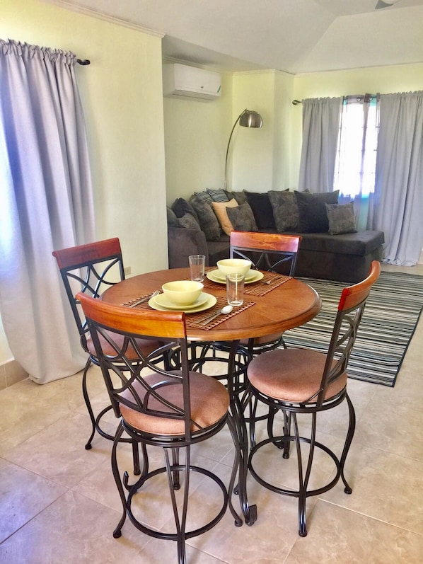 A dining area with a round wooden table, four chairs, and a sofa in the background.
