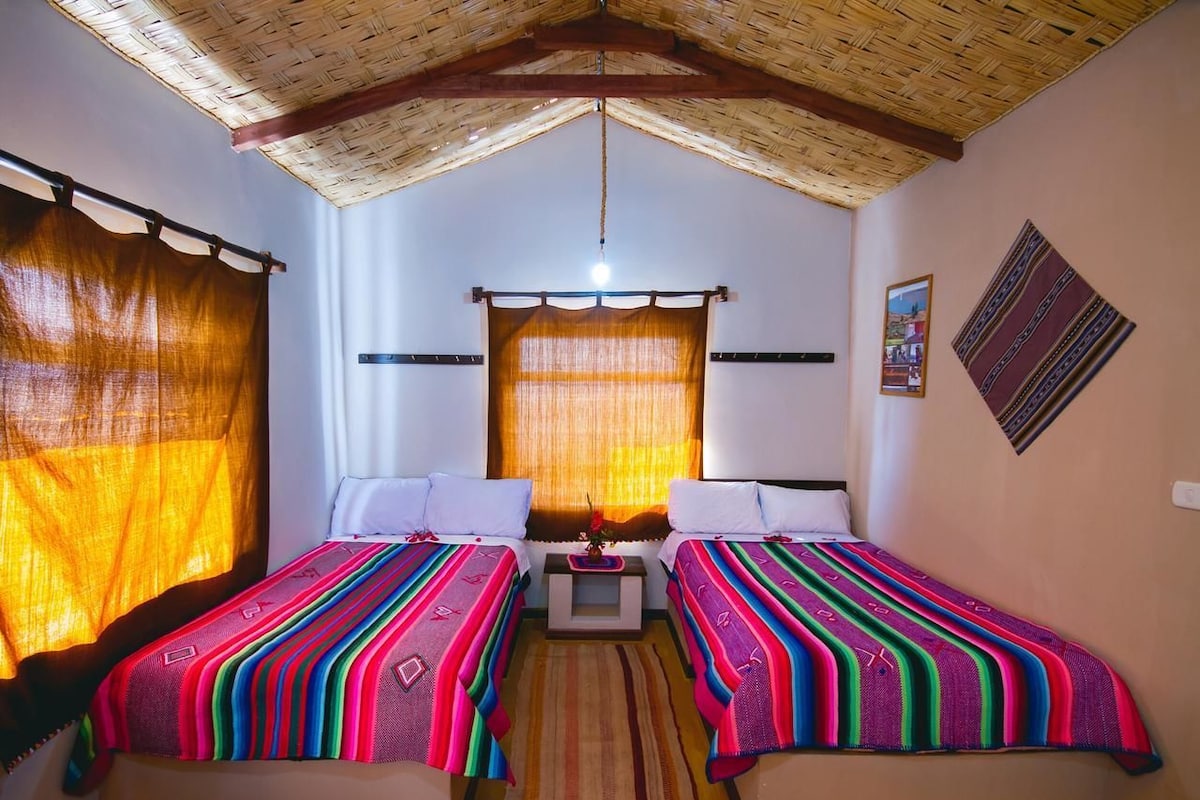 A room with two beds, a small table, and a hanging light fixture.