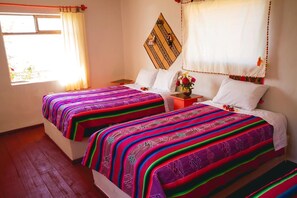 A room with two beds, each with colorful striped bedding. There is a small table with a vase of flowers between the beds. - Suma Luquina (Chucuito)