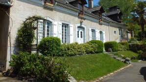 A traditional building with multiple windows and a balcony, surrounded by well-maintained greenery and a stone pathway. - Chambres d'hôtes Anousta (Loubajac)
