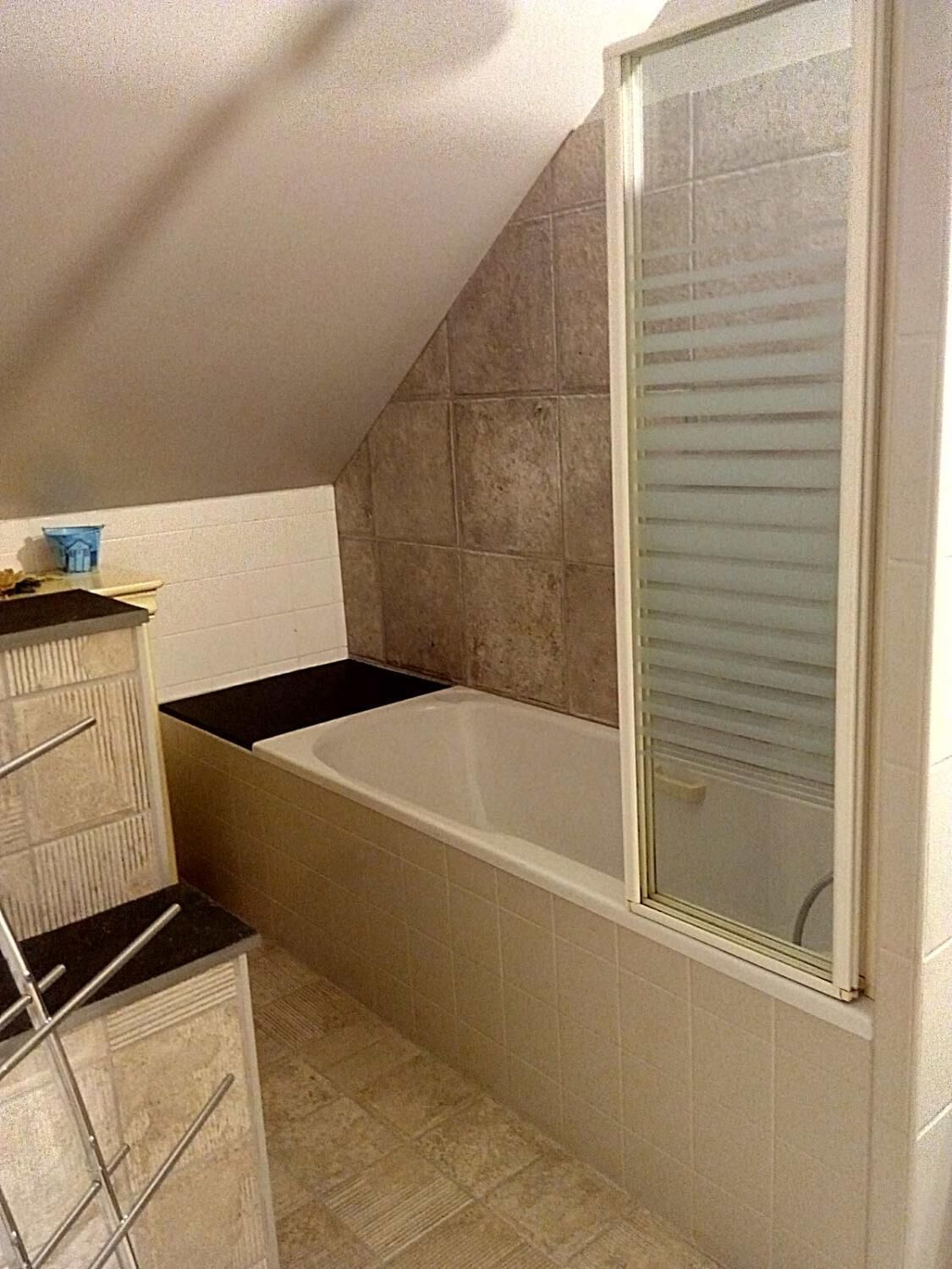 Een kleine, smalle badkamer met een bad, een douche en een betegelde vloer.