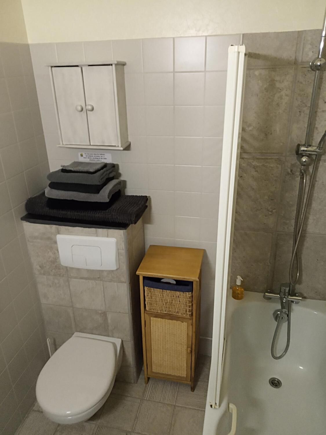 Ein Badezimmer mit Toilette, einer kleinen Ablage, einem Korbwäscheschrank und einer Duschkabine.