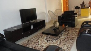 A living room with a black sofa, a flat-screen TV on a black cabinet, a patterned rug, and a coffee table. - Residence Yoff Toundou Bya (Dakar)