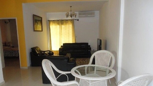 A living room with a black sofa, a glass coffee table, and white wicker chairs. - Residence Yoff Toundou Bya (Dakar)