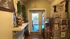 A hallway with an exit sign, a greeting card display, and a small plant on the left.