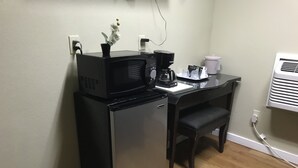 A compact kitchenette with a refrigerator, microwave, coffee maker, and a small table with a chair.