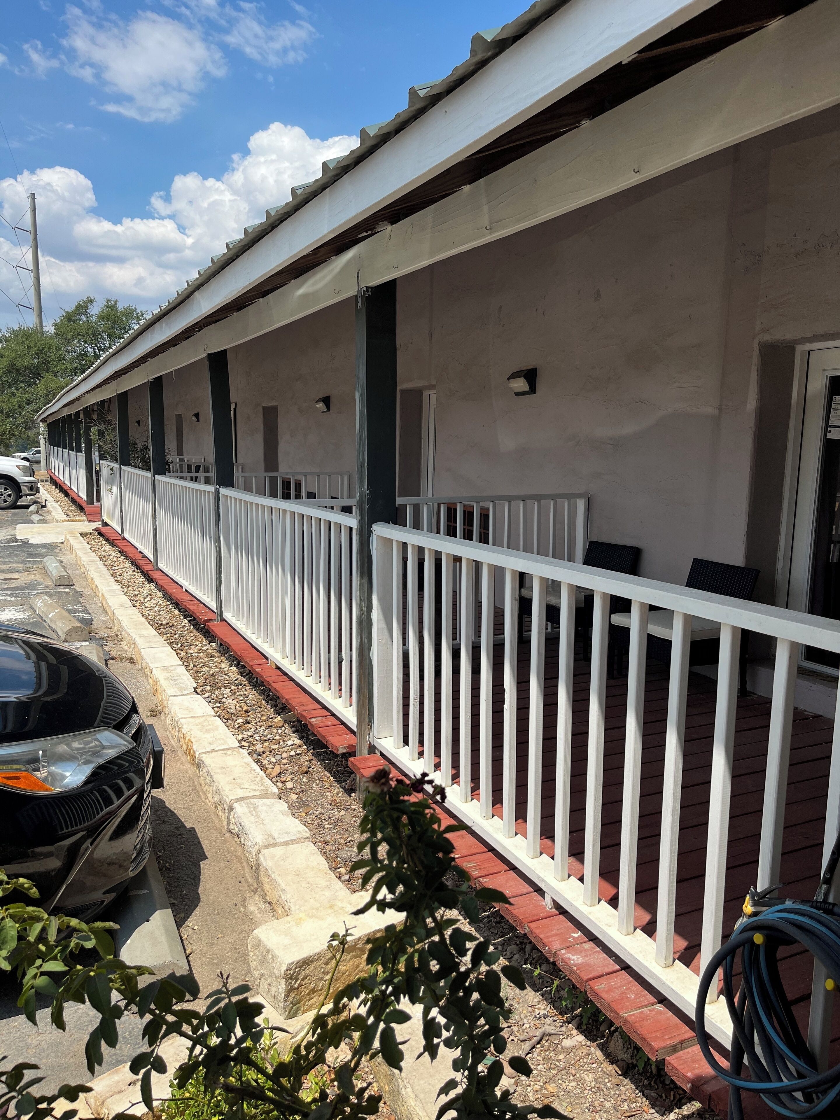 A long, single-story building with a covered outdoor area, white railings, and a paved walkway.