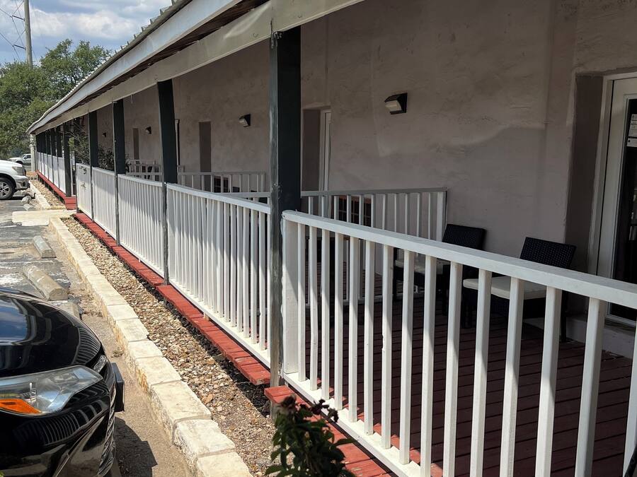 Um edifício baixo e alongado, com área externa coberta, corrimãos brancos e um calçadão pavimentado.