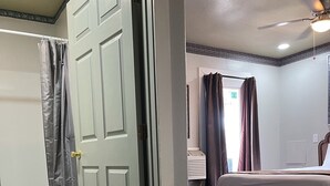 A hotel room with a bed, a ceiling fan, and a bathroom with a shower curtain.