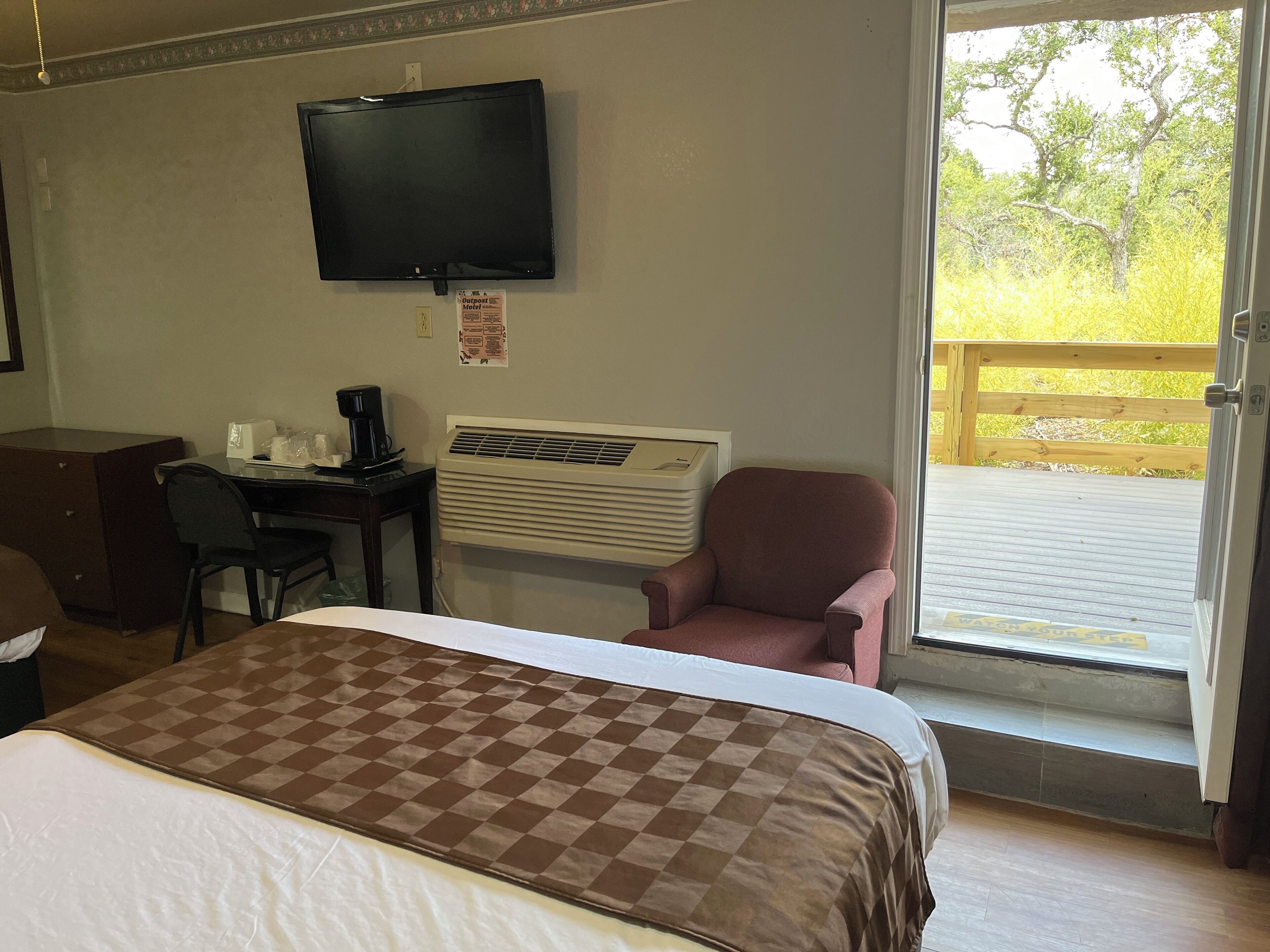 A hotel room with a bed, a desk with a computer, a chair, an air conditioner, and a TV on the wall.