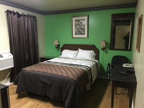 A hotel room with a bed, a desk, a chair, a telephone, and a picture on the wall.