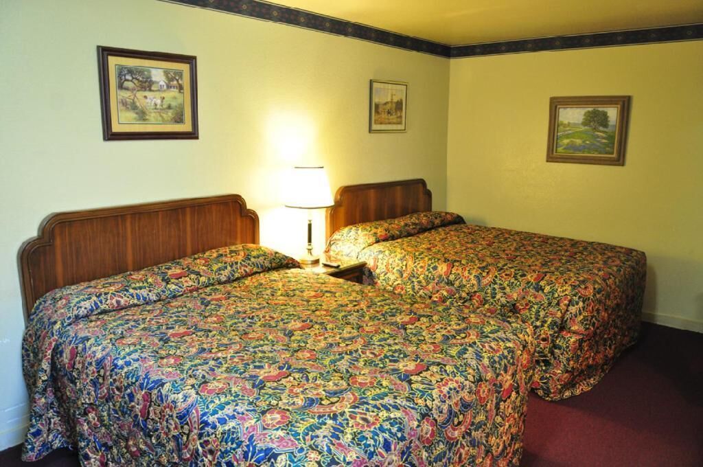 Une chambre d’hôtel avec deux lits, une lampe et des tableaux encadrés aux murs.