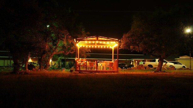 A gazebo with string lights, surrounded by trees and parked cars.