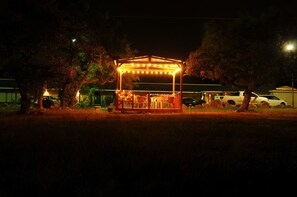 A gazebo with string lights, surrounded by trees and parked cars. - Outpost Motel (Dripping Springs)