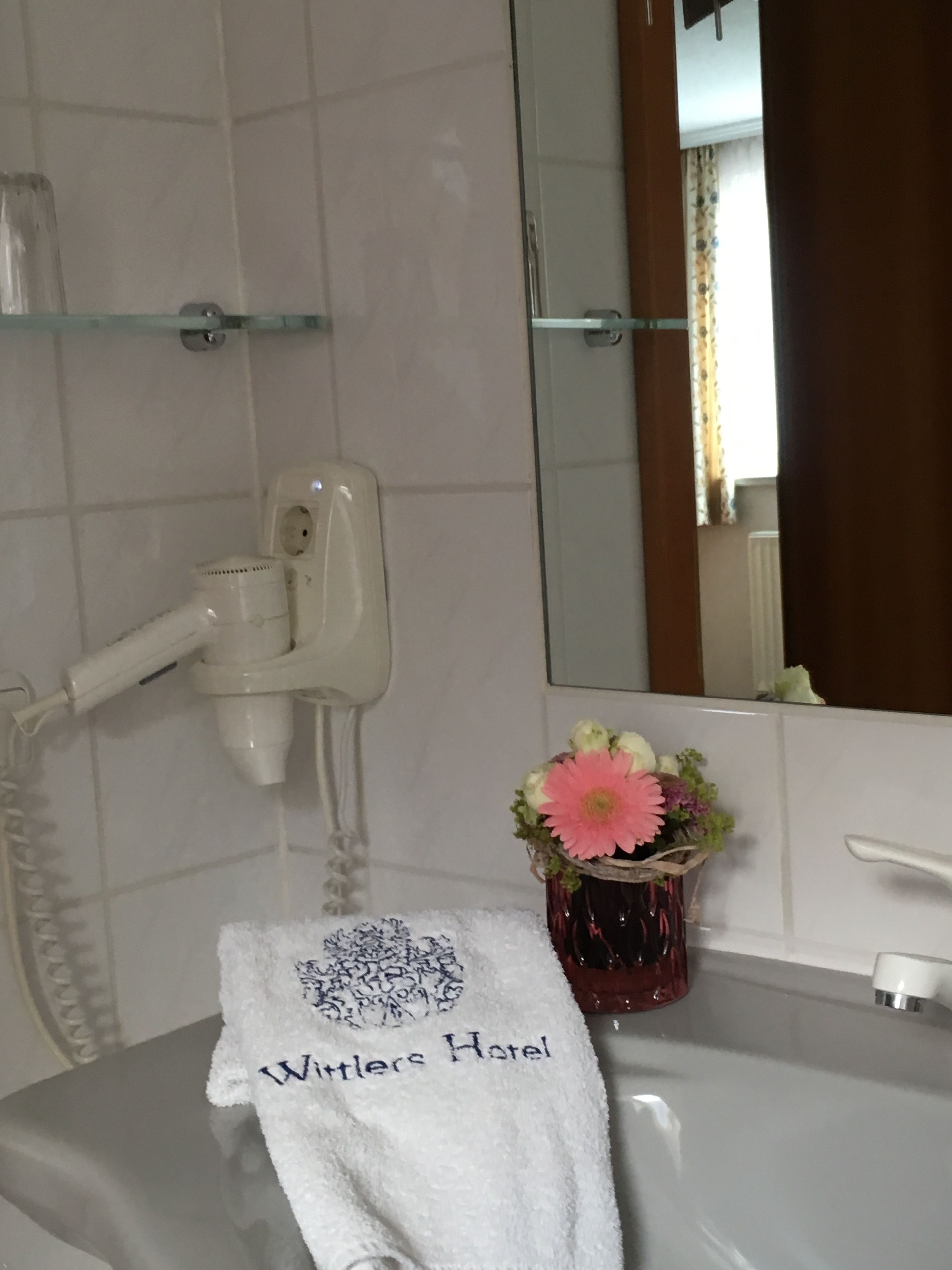 Ein Badezimmer mit einem weißen Waschbecken, einem Handtuch mit der Aufschrift "Winter's Hotel" und einer Vase mit Blumen. Darüber hängt ein Spiegel.