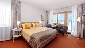 A hotel room with a large bed, a desk, a chair, a TV, and a window with a view. - Wittlers Hotel (Ratzeburg)