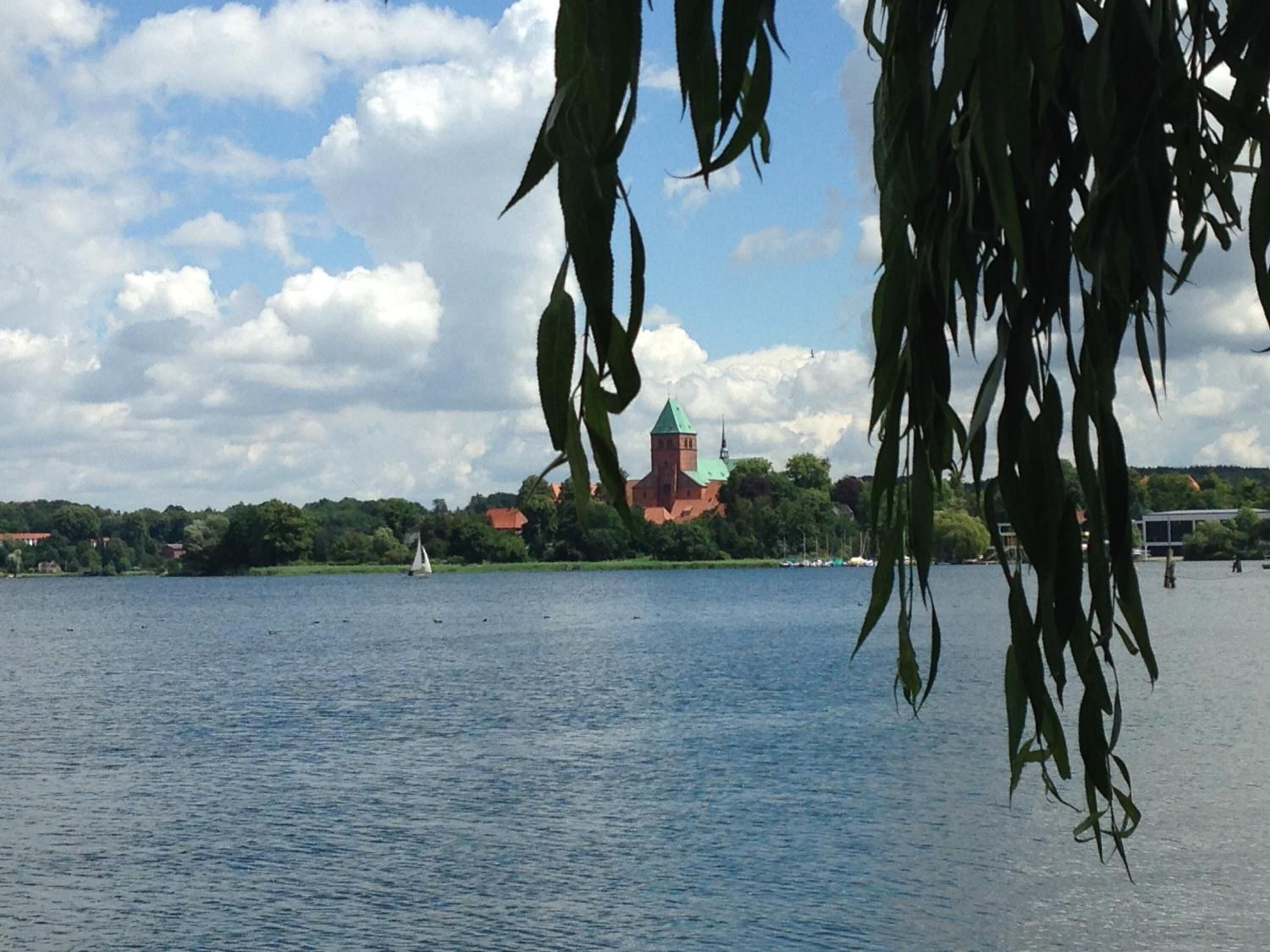 A calm lake with a church and sailboat in the distance.