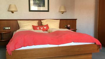 A hotel room with a wooden bed, two bedside lamps, a nightstand with a clock, a framed picture on the wall, and a red throw blanket.