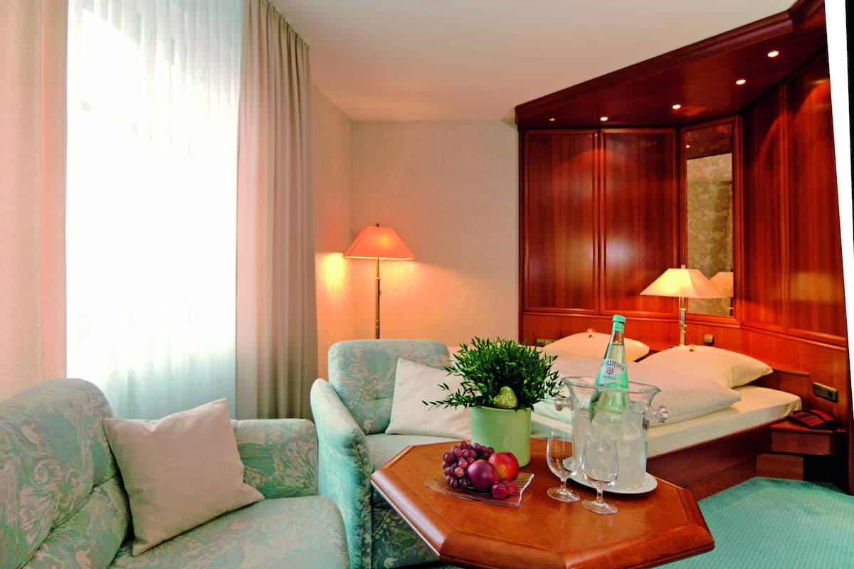 A hotel room with a bed, a sofa, a coffee table with fruit and a bottle, and a lamp.
