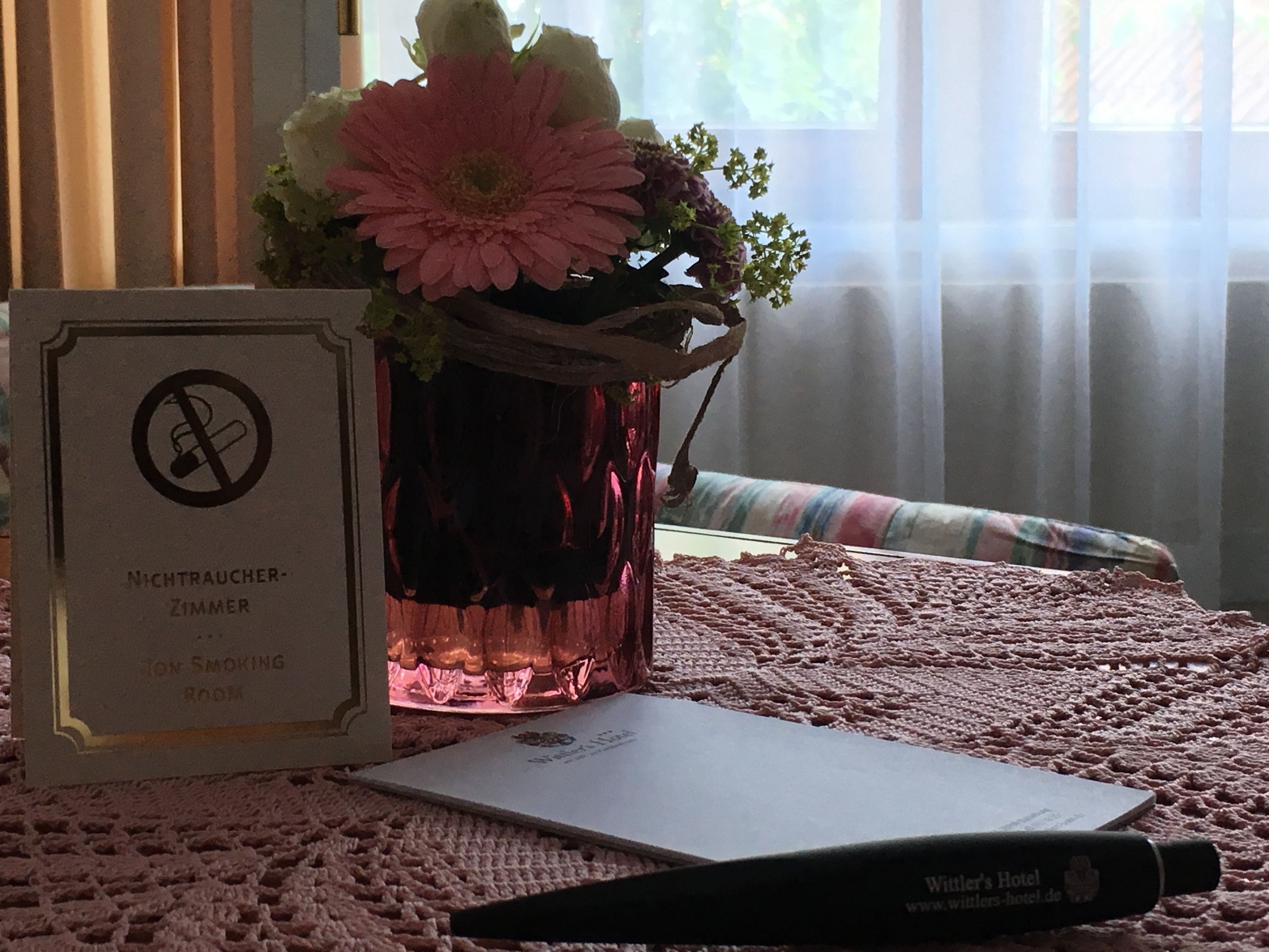 A room with a sign indicating it is a non-smoking room, a vase with flowers, a notebook, and a pen on a textured surface.