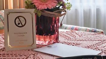 Hotelkamer met een ‘Niet roken’-bord, een roze vaas met bloemen, een laptop en een pen op een roze tafelkleed met textuur.