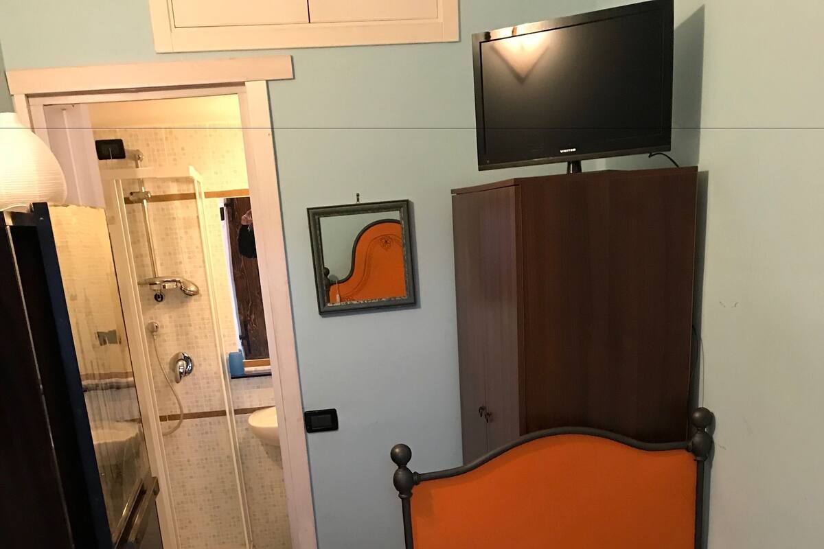 Een slaapkamer met een bed, een stoel, een kledingkast, een televisie en een badkamer zichtbaar door een geopende deur.