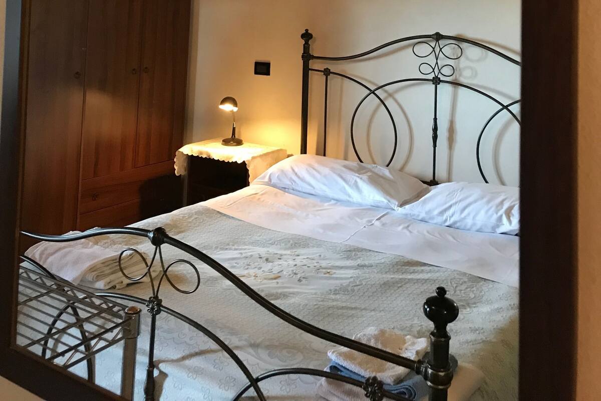 Een slaapkamer met een houten plafond, een metalen bedframe, een nachtkastje met een lamp en een kledingkast.
