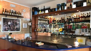 Een bar met een toonbank, planken vol drankflessen en een lijst op de muur.
